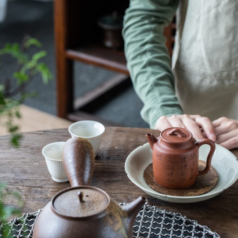 Théière en terre cuite et tasses sur une table en bois, ambiance chaleureuse.