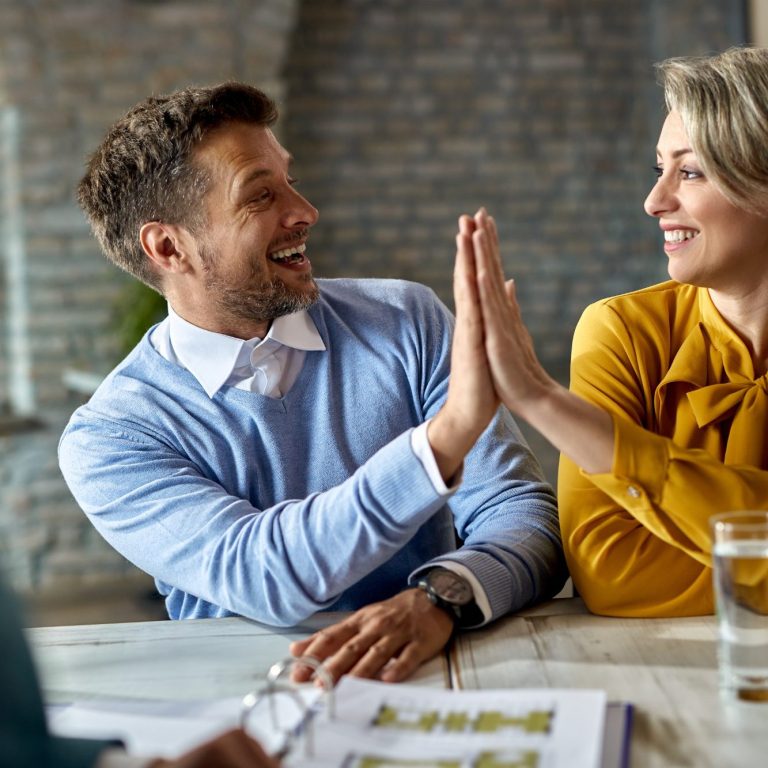 Deux collègues se félicitent avec un high five, souriant, dans un bureau moderne.