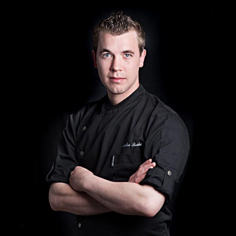 Chef en uniforme noir, bras croisés, regardant vers l'objectif.