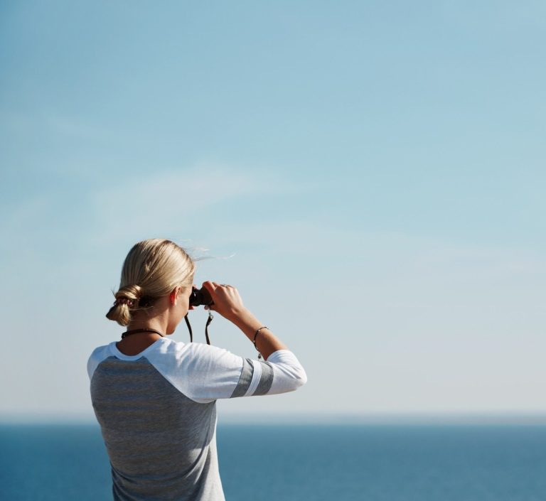 Femme regardant l'horizon avec des jumelles au bord de la mer.